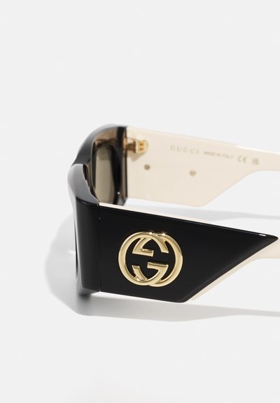 Svarta plastsolglasögon med en guldfärgad Gucci-logotyp, vinklad design och gradientfärgade linser med kravita glasögonarmar.