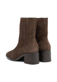 Las botas de ante marrón hasta el tobillo presentan un diseño de costuras verticales, una punta redondeada y un tacón grueso con una superficie texturizada.