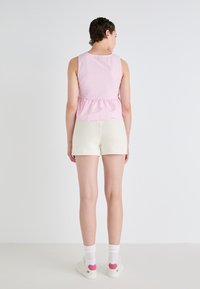 Roze en witte gestreepte mouwloze top in peplumstijl, gecombineerd met witte textuuroverhemden. Schoeisel: witte sneakers met roze accenten.