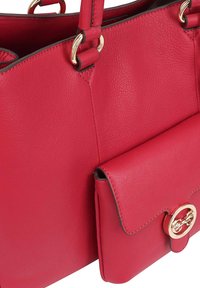 Rode leren tas met een gestructureerde textuur, voorzien van vergulde hardware en een voorvak dat is beveiligd met een ronde sluiting.