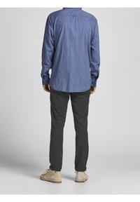 Knapp-up skjorta i denimblått tyg, lång ärm, rundad nederkant, tillsammans med mörka byxor och beige mockaskor, sedd bakifrån.