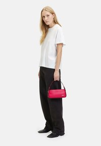 Borsa a tracolla rossa in pelle, di forma rettangolare e con manico superiore, abbinata a una maglietta bianca e pantaloni ampi neri. Texture liscia, hardware minimal.