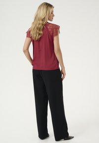 Burgunditopp med spets�ärmar, kombinerad med svarta vida byxor. Outfiten har en jämn textur och en avslappnad passform.
