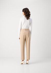 Beige kalhoty na míru se střihovým provedením rovného nohavice, dvěma zadními kapsami a hladkým povrchem, doplněné světle zbarvenými podpatky.