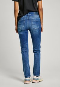 Jean en denim bleu slim fit avec une taille moyenne, poches arrière et décoloration subtile. Associé à des chaussures de sport multicolores.