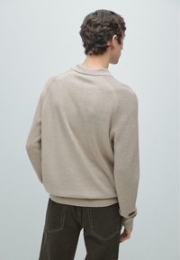Maglione beige lavorato a maglia con collo a coste, orlo rotondo e maniche lunghe, abbinato a jeans scuri. Tessuto liscio e vestibilità comoda.