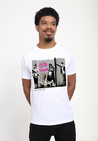 Bílý bavlněný tri�čko s grafickým potiskem čtyř postav v černobílé barvě a růžovým textem "OLD skool." Jednoduchý design s kulatým výstřihem.