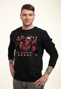 Sudadera negra con un gráfico colorido de un personaje con un gorro de Santa, rodeado de patrones navideños en rojo y blanco.
