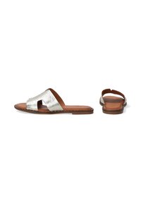 Metallic zilveren slapsandalen hebben een open teenontwerp, een zachte bruine leren voetbed, een platte zool en minimale stikdetails.