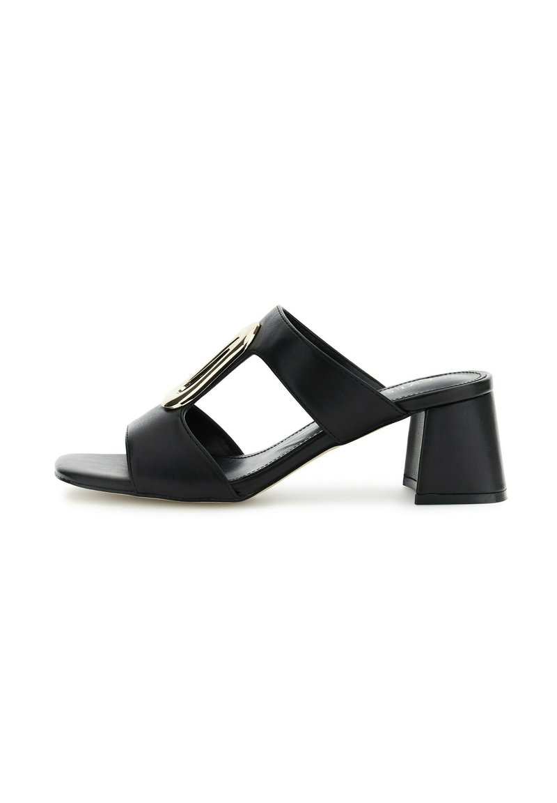 Mules de piel negra con tacón, con un diseño recortado y un acento dorado. Presentan una punta cuadrada y un tacón grueso y acampanado. Textura suave.