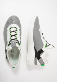 Des chaussures de sport grises avec une tige texturée, des accents blancs, des lacets verts et des sangles noires. Elles disposent d'une semelle rembourrée et d'un design perforé.