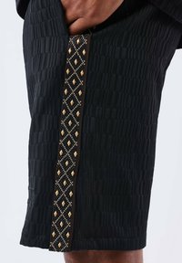 Black shorts with a textured pattern, featuring a decorative side strip with diamond-shaped gold accents and beads.