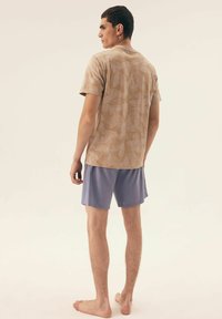 Brązowa koszula z krótkim rękawem w liście, w połączeniu z jasnofioletowymi szortami. Tkanina mieszanka bawełny, luźny krój, miękka tekstura.