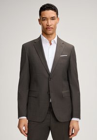 Completo grigio scuro con un tessuto strutturato. Presenta un risvolto a punta, due tasche frontali, una chiusura a singolo bottone e una camicia bianca sotto.