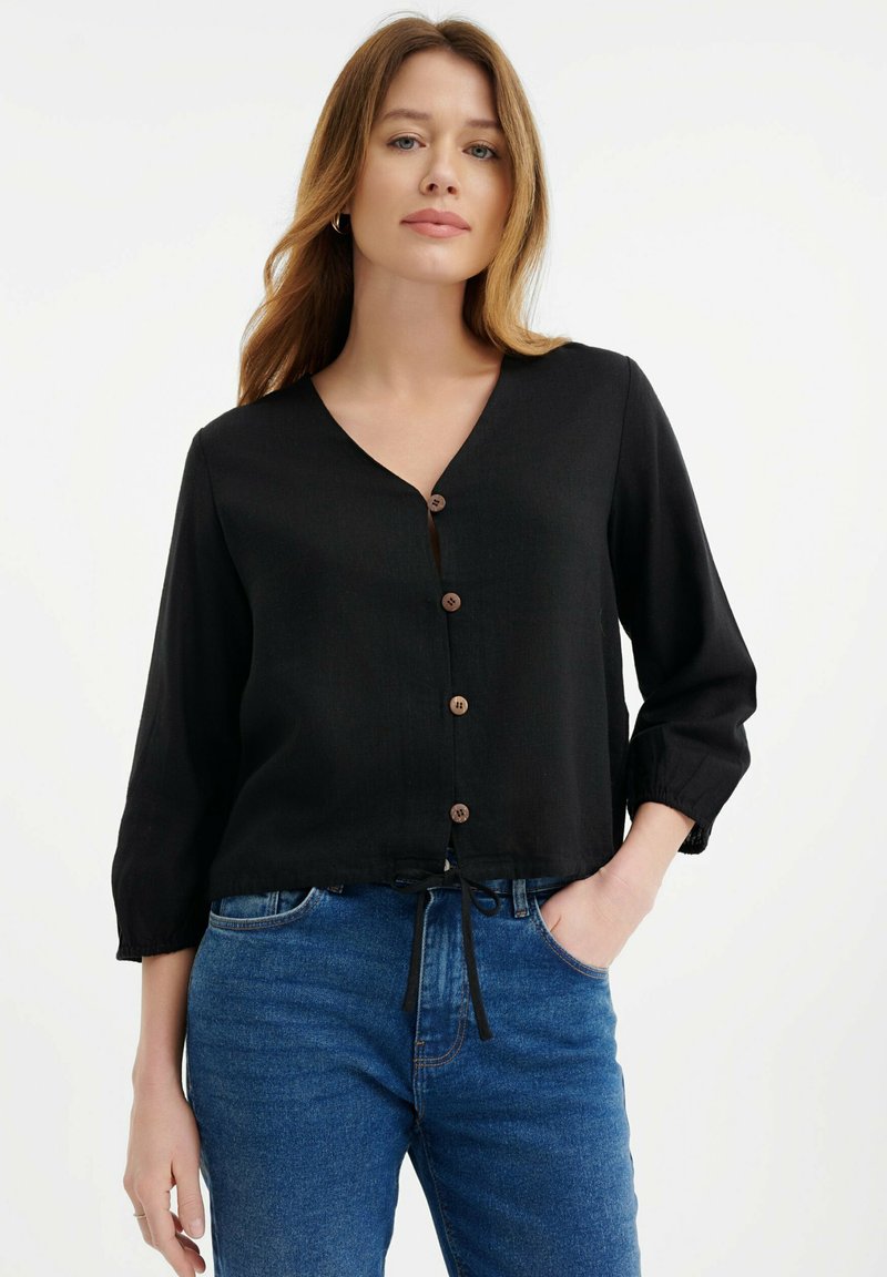 Zwarte overhemd met V-hals en lange mouwen, voorzien van houten knopen, een strik in de taille en een relaxte pasvorm. Denim jeans zijn zichtbaar.