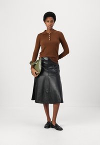 Maglione marrone a maglia con colletto con bottoni, abbinato a una gonna midi in pelle nera e mocassini scuri. Una borsa a tracolla verde completa l'outfit.