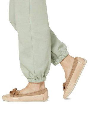 Zapatos planos en tonos beige y tostado, fabricados en cuero y ante, con un lazo en la puntera y suela de goma blanca; combinados con joggers de color verde claro.