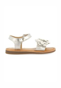 Sandal in metallo argento con suola piatta marrone, cinturino regolabile e decorazione floreale sulla punta. Texture liscia, design minimalista.
