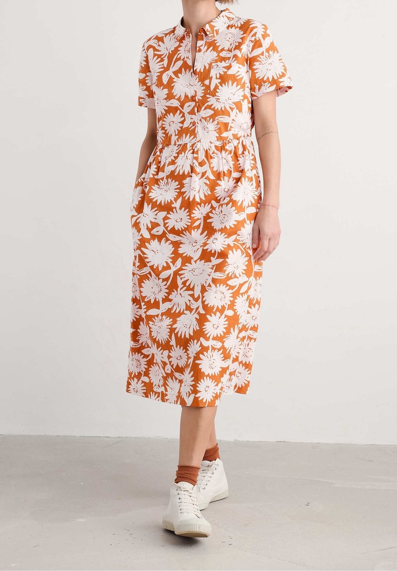 A knee-length dress in orange with a white floral pattern, featuring short sleeves, a buttoned neckline, and side pockets.