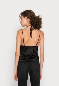 Top preto em satin com alças finas ajustáveis, costas franzidas e um laço no pescoço, apresentando uma textura suave e um design minimalista.