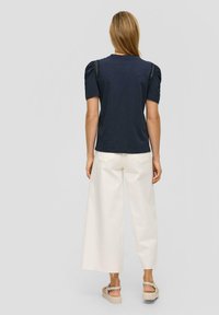 Navyblauwe t-shirt met korte, geplooide mouwen en geweven accenten. Gepaard met een wijde crèmekleurige broek en tan platform sandalen.