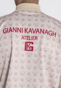 Lichtroze jack met een herhaald beren- en "K"-logo print, met rode tekst die "GIANNI KAVANAGH ATELIER" op de achterkant leest.