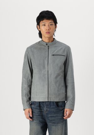 Jacket de ante gris con cuello alzado, cremallera frontal y un bolsillo en el pecho. Presenta detalles de costura sutiles y un corte entallado.