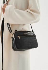 Borsa a tracolla nera in pelle effetto coccodrillo con dettagli dorati, due scomparti con zip e una tracolla regolabile. Design compatto e rettangolare.