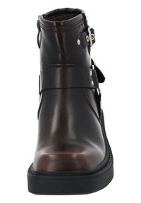 Bota de tobillo de cuero marrón con acabado suave, herrajes plateados, correa decorativa y puntera redonda. Presenta una suela de goma baja.