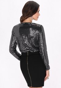 Top lungo a maniche nere con paillettes abbinato a una gonna nera aderente con una cerniera visibile sul retro. Texture lucida, design elegante.