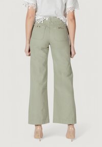 Pantaloni a gamba larga, di colore verde chiaro, realizzati in cotone, con vita alta, due tasche posteriori e una consistenza liscia. Abbinati a un top bianco con orlo in pizzo.