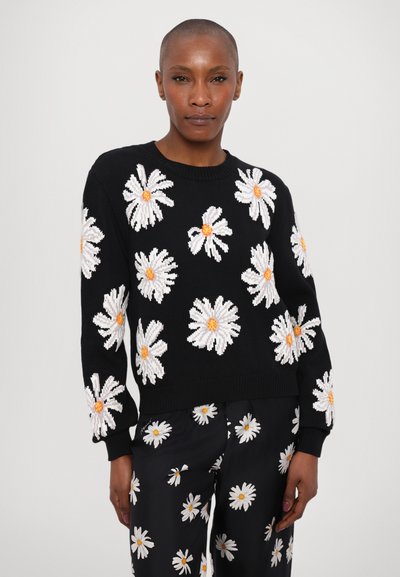 Schwarzer Strickpullover mit gestickten weißen Gänseblümchen, die orangefarbene Mittelpunkte haben. Langärmlig, mit gerippten Bündchen und Saum. Kombiniert mit einer Hose im Gänseblümchenmuster.