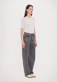 Top corto de manga corta blanco con canalé, combinado con unos vaqueros de mezclilla negros de pierna ancha y cintura alta. Textura suave con un sutil detalle de desgaste.