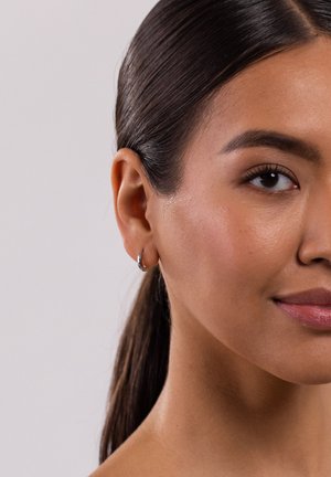 Silberne Creolen an einem Modell mit glatter Haut, dunklem zurückgebundenem Haar und neutralem Lippenfarbton. Der Fokus liegt auf der Form der Ohrringe.