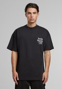 Black cotton oversized t-shirt featuring a white text print "Sunday Running Club" on the left chest area. Short sleeves and crew neck design.