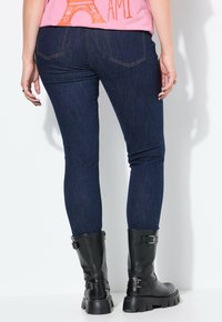 Jeans skinny azul oscuro con una textura suave, que cuentan con dos bolsillos traseros y costuras contrastantes, combinados con botas negras hasta la mitad de la pantorrilla.