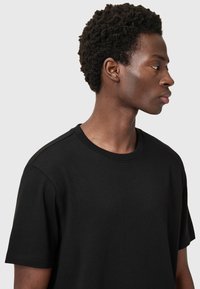 T-shirt nera in cotone con colletto a giro e maniche corte, dal tessuto morbido e design minimalista. Nessun motivo o dettaglio visibile.
