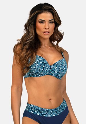 Kobieta o długich, falujących włosach, ubrana w niebieski wzorzysty top od bikini i górę bikini o wysokim stanie w jednolitym niebieskim kolorze, na jednolitym tle.