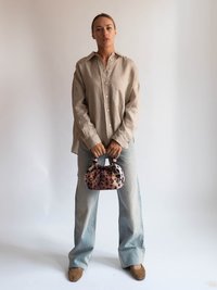 Camicia di lino beige con bottoni, jeans a gamba larga azzurri, ballerine in suede marrone e una piccola borsa a tracolla leopardata con parte superiore arricciata.