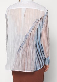 Genomskinlig, lätt blus med plisserad textur, ett färgstarkt abstrakt tryck i blått och beige, samt en klassisk krage med knappstängning.