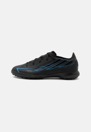 Crampon de sport noir avec des touches bleues, des lacets et une semelle texturée conçue pour les sports sur gazon synthétique.