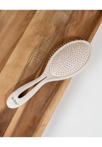 Beige umweltfreundliche Haarbürste mit Kunststoffborsten und strukturierter Grifflage auf einer Holzoberfläche.
