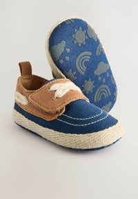 Bottes en toile bleue avec une sangle en tissu marron, des coutures blanches et une semelle de couleur claire. La semelle présente un motif bleu de soleil, de nuages et d'arcs-en-ciel.