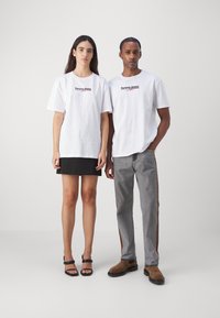 Camisetas blancas con el logo de "Tommy Jeans" en rojo, combinadas con una falda negra y pantalones gris claro con rayas laterales. Sandalias negras y botas marrones.
