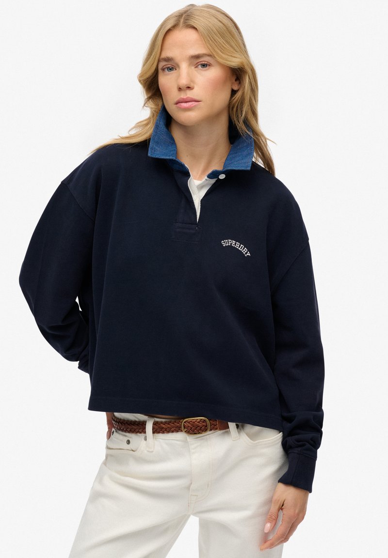 Sweatshirt bleu marine avec un col en denim, arborant un logo brodé blanc et une coupe décontractée. Manches longues et design court.