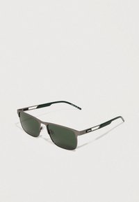 Gafas de sol con un elegante marco rectangular de metal, lentes verdes y puntas de las patillas en verde oscuro con un sutil logo en el lateral.