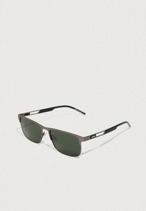 Occhiali da sole con una montatura metallica rectangular elegante, lenti verdi e punte delle tempie verde scuro con un branding discreto sul lato.