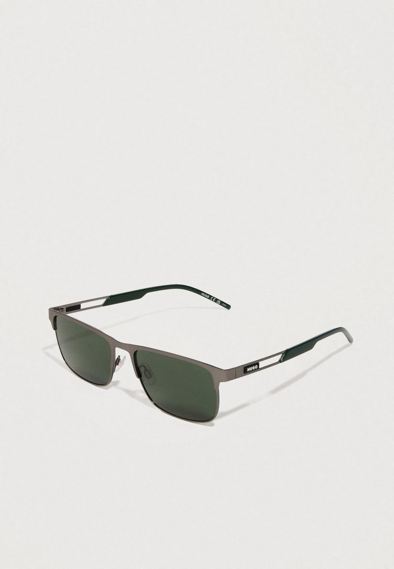 Gafas de sol con un elegante marco rectangular de metal, lentes verdes y puntas de las patillas en verde oscuro con un sutil logo en el lateral.