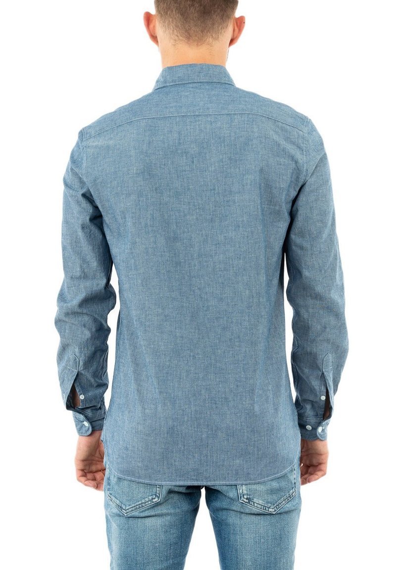 Camicia di jeans azzurro chiaro con maniche lunghe, polsini con bottoni e colletto classico. Presenta una texture liscia e una vestibilità sartoriale.