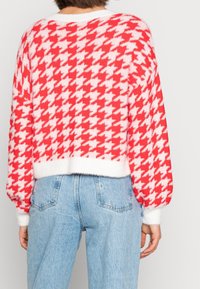 Sweter w czerwono-biały wzór pepitki o krótkim kroju, puszystej fakturze i szerokich rękawach, zestawiony z niebieskimi dżinsami z wysokim stanem.